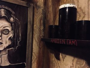 In-game: half of a creepy portrait of a woman beside a shelf with jars labeled "ambien."