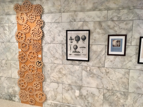 In-game: a tower of interlocking wooden gears against a marble museum wall.