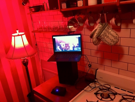In-game: A laptop sitting on a counter in a red lit kitchen.