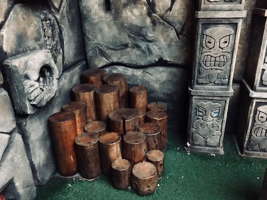 In-game: stone walls and pillars beside a collection of tree stumps.