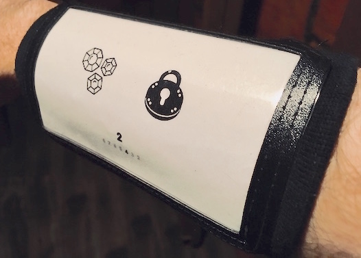 In-game: close up of a wrist cuff with a series of symbols.