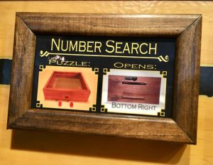 In-game: a framed puzzle description labeled "Number Search." It shows the puzzle component and the box that it opens.