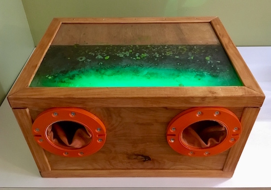 In-game: a sealed box filled with glowing green material and mounted gloves.