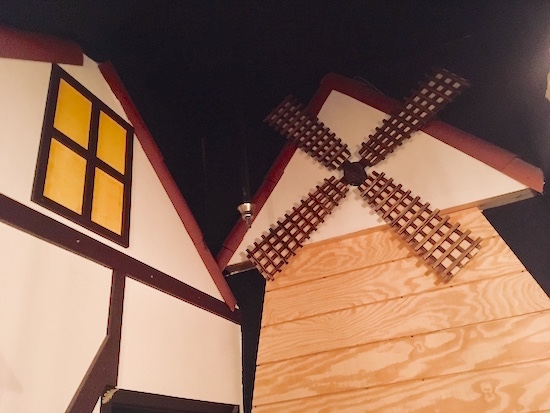 In-game: a view of the exterior of a home adjacent to a windmill.