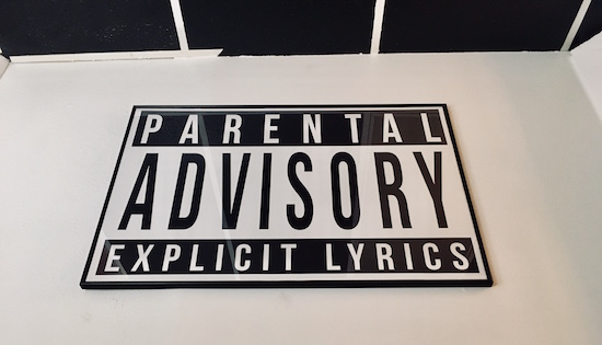 In-game: a large Parental Advisory Explicit Lyrics poster hanging on the wall.