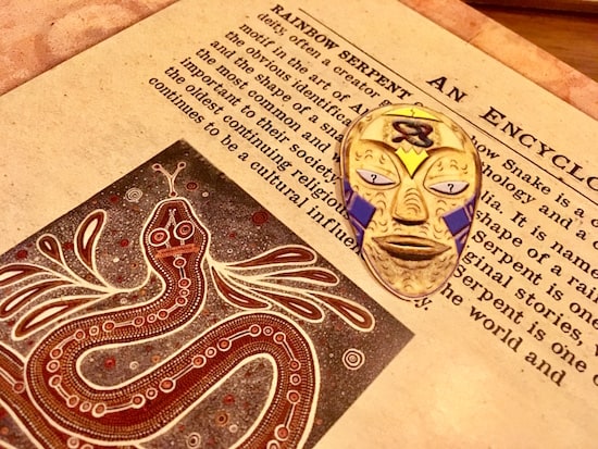 In-game: A colorful Aboriginal mask over a text about the myth of the Rainbow Serpent.