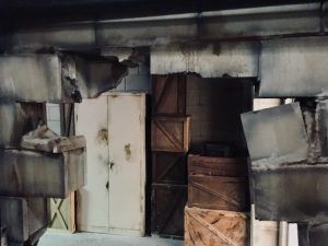 In-game: A hole in a wall, a storage room with crates is beyond it.