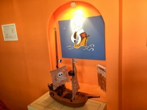 In-game: A Playmobile pirate ship on a table under a painting of a pirate ship.