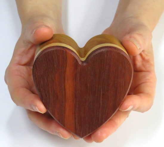 Two hands holding a heart shaped wooden box.