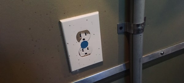 An electrical outlet with a blue do not touch sticker.