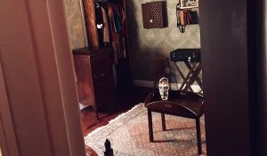 In-game: View through the door of Do Not Disturb into a studio apartment with a creepy doll sitting on a table in the middle of the room.