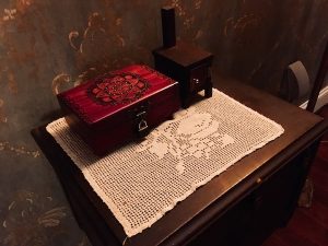 In-game: a small table two two unusual wooden locked boxes.