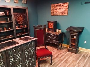 In-game: wide shot of the apothecary. There is a large red chair and a lectern.