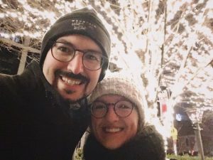 Lisa and David bundled up in front of a tree covered in lights.