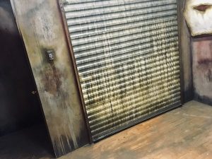 In-game: the heavily weathered garage door with a digital keypad beside it.