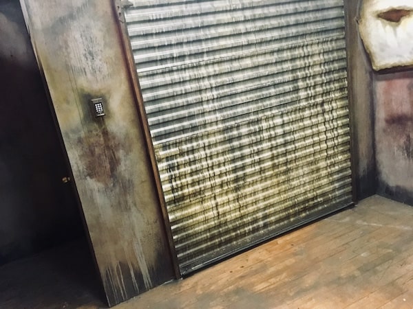 In-game: the heavily weathered garage door with a digital keypad beside it.