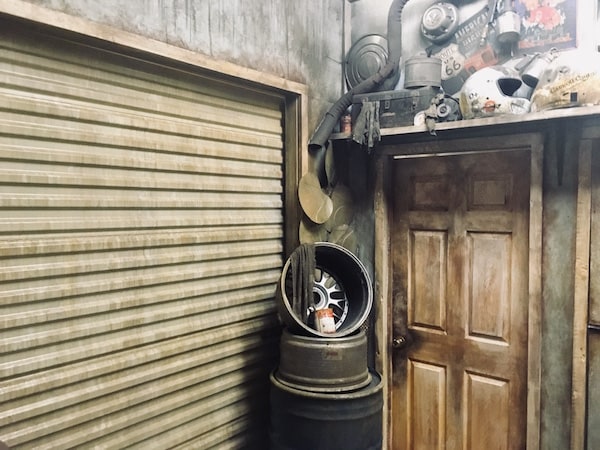 The exterior entrance/ exit for The Garage. A weathered door and garage door surrounded by car parts.