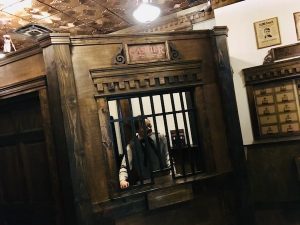 In-game: A cashier standing behind a barred window in an elegant wooden bank.