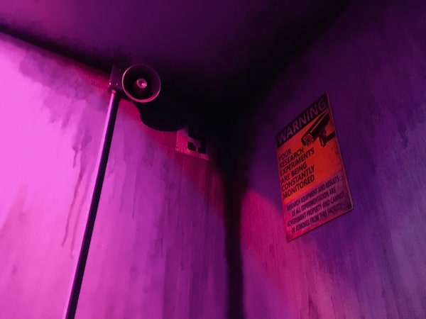 In-game: A PA mounted near the ceiling of the bunker. There's a sign warning of surveillance.