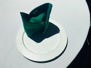 In-game: A neatly folded green napkin on a white plate and white tablecloth.