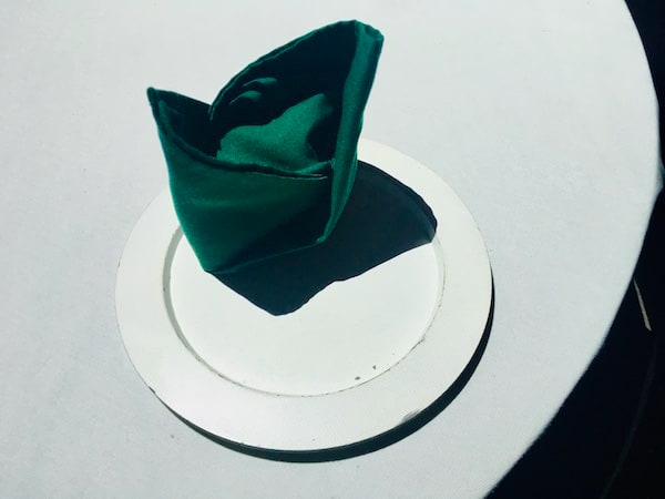 In-game: A neatly folded green napkin on a white plate and white tablecloth.