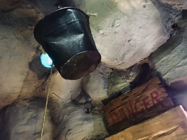 In-game: A bucket hanging from a rope in a mine. There is a wooden sign labeled "DANGER" hanging from the wall.