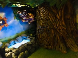 In-game: The Cheshire Cat hanging in a big tree branch over a pool of water.