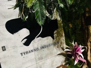 In-game: The Tryanno Industries logo on a concrete building in a tropical setting.