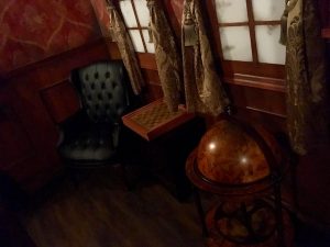 In-game: A chair beside a chess table and a globe in a study.