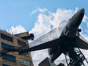 An airplane suspended in air, and a bus hanging off the roof of the building.