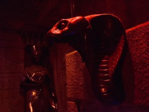 In-game: A statue of a cobra's head protruding from the sandstone wall of a tomb.