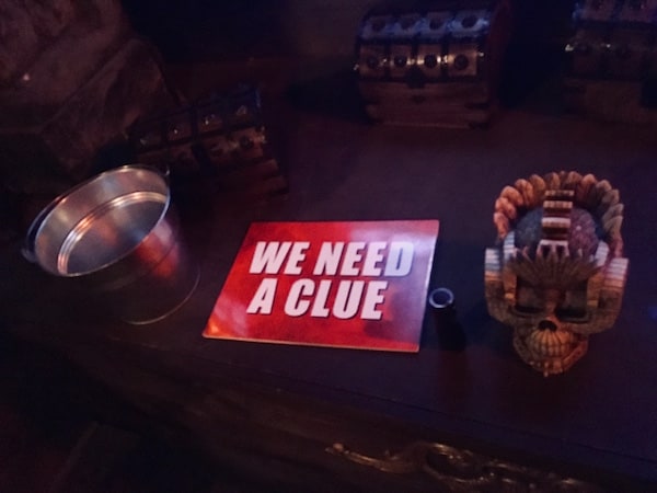 In-game: A bright "we need a clue" sign beside a flashlight, an ornate skull, and many small treasure chests.