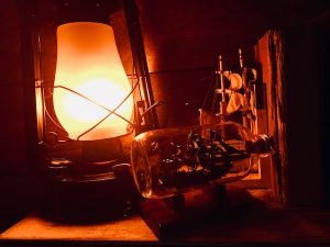 In-game: Closeup of a shelf with a lantern and a ship in a bottle.