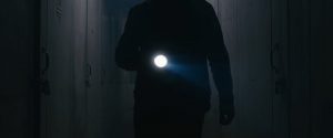 Closeup of a man with a flashlight searching a hallway of storage units.