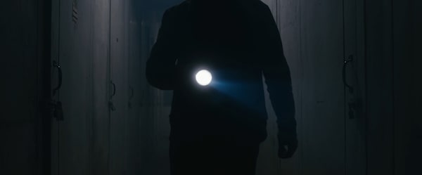 Closeup of a man with a flashlight searching a hallway of storage units.