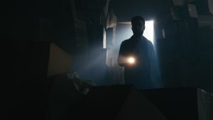A man with a flashlight searching a storage space filled with cardboard boxes.