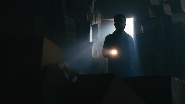 A man with a flashlight searching a storage space filled with cardboard boxes.