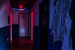 In-game: The hallway of an asylum with patient clothes hanging from hooks on the wall with the lights turned down.