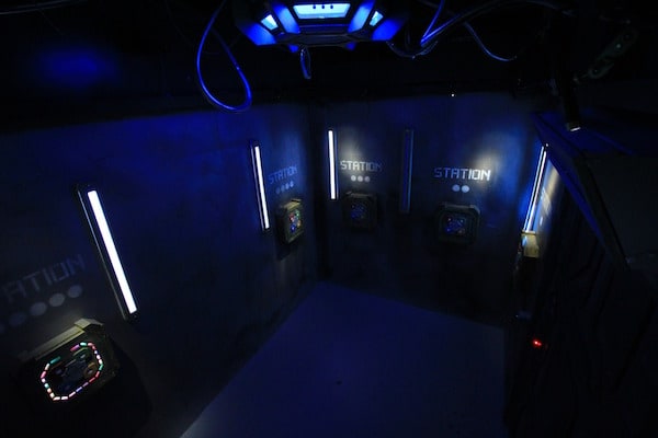 In-game: Wide angle shot of a room with access terminals along the walls.