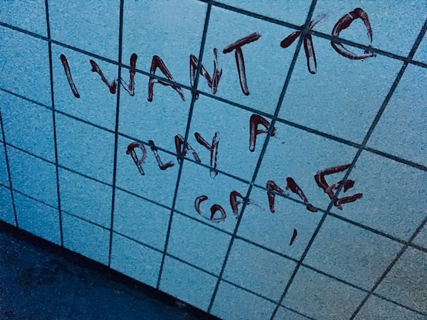 In-game: "I want to play a game" painted in blood on a white tiled wall.