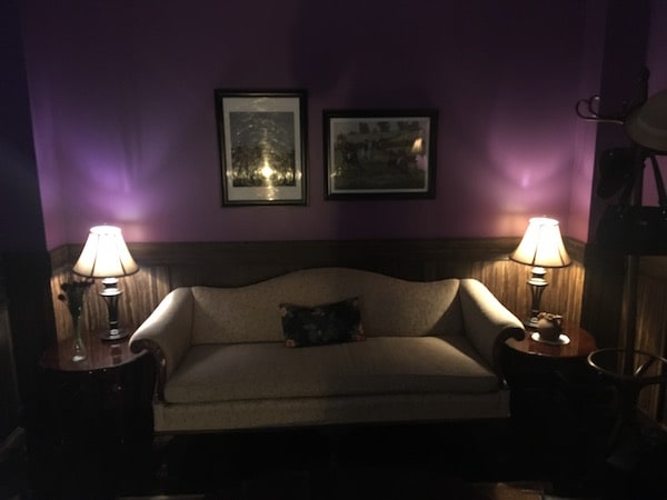 In-game: A purple walled study with a couch flanked by table lamps.