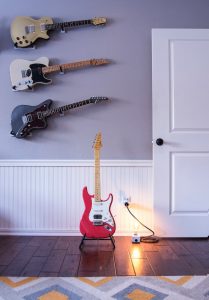 A room with 4 electric guitars, a single light bulb, and a door.
