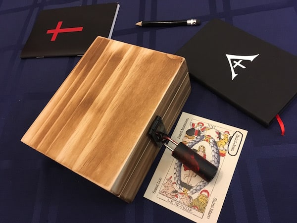 A wooden lockbox, with a bloodied lock beside a bible and a notebook.