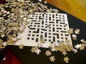 Loose jigsaw pieces surrounding a paper crossword puzzles.