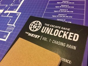 Closeup of the game's rules, a small notebook, and a set of blueprints.