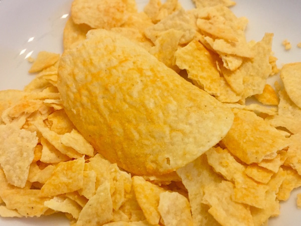 One whole, unbroken mystery flavor Pringle resting on a bed of broken chips. The chips have an orangey appearance.