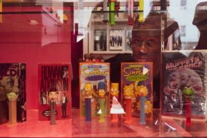 A person reaching into a display case with movie boxes and pez dispensers that correspond to the characters featured on those boxes.
