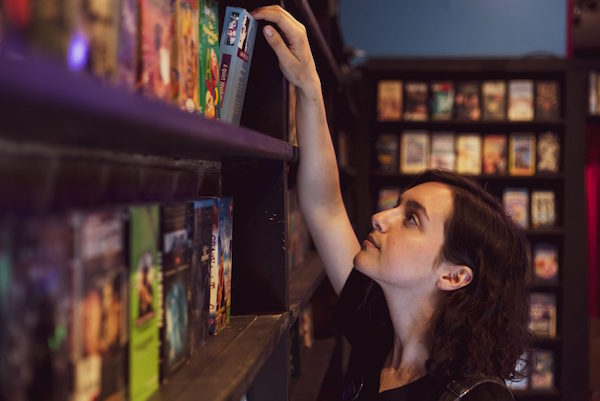 A person reaching up for a movie on the shelf of a video store.