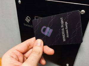 In-game: a "MINERVA Project Access Badge" held up to a scanning station.