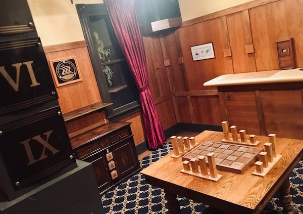 In-game: wide shot of the room, a strange game sits on a table in the middle of the room.